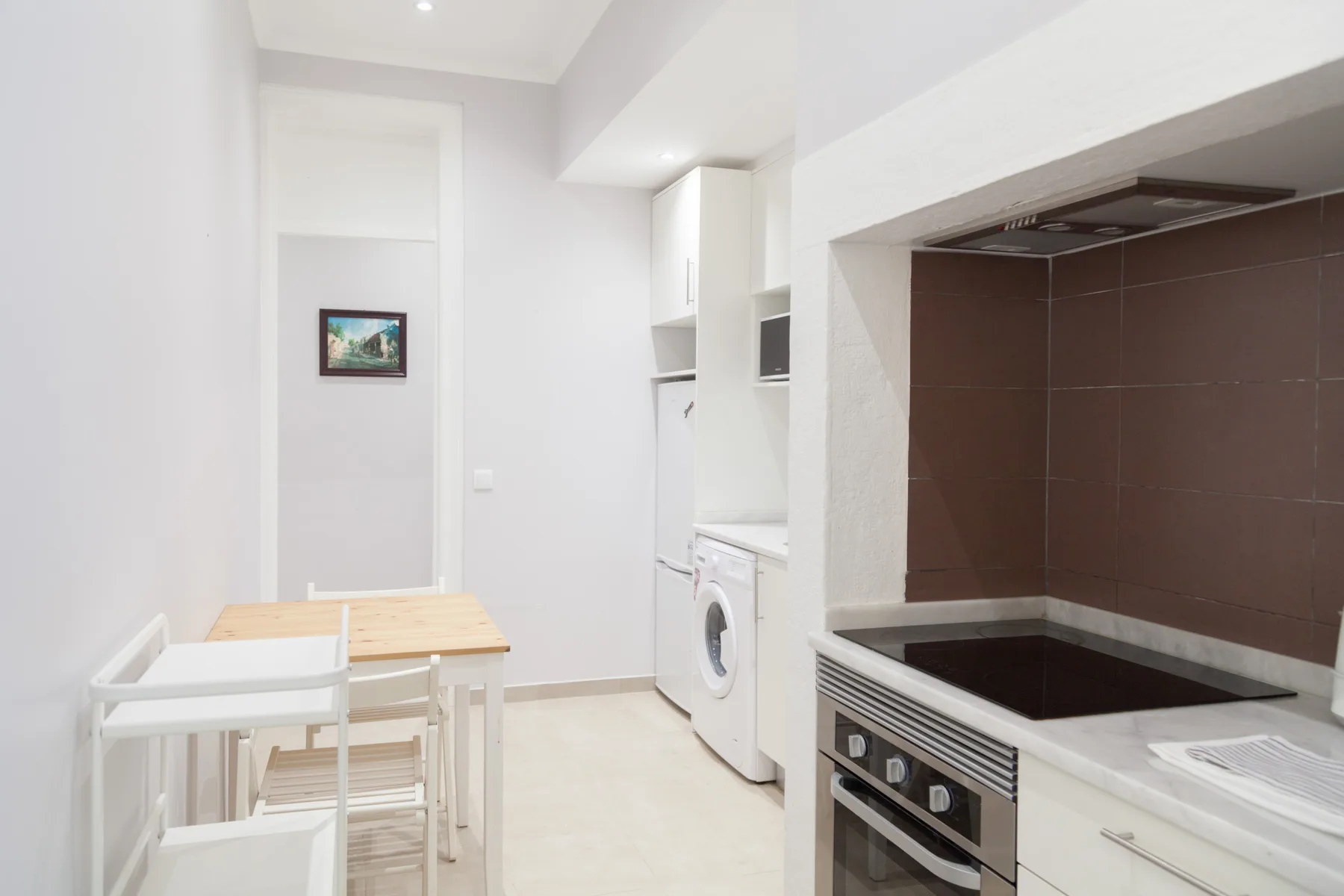 Una cocina compacta con zona de comedor, placa, horno y mesa pequeña.