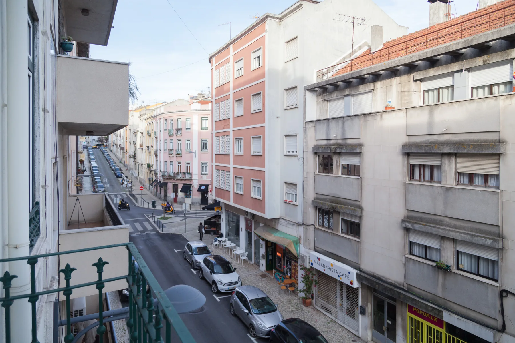 Una calle urbana bordeada de edificios de varias plantas y coches aparcados.