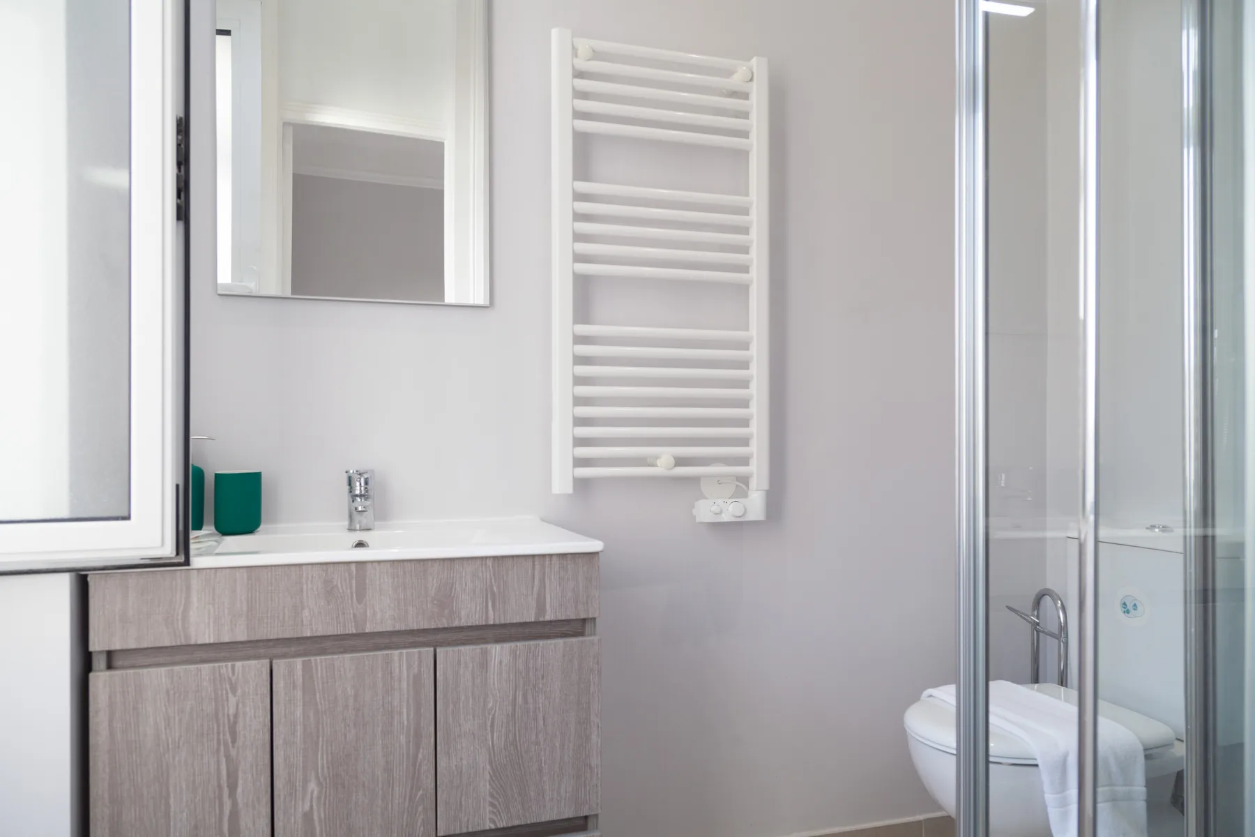 Un baño luminoso con lavabo, toallero calefactable en la pared y ducha con mampara de vidrio.