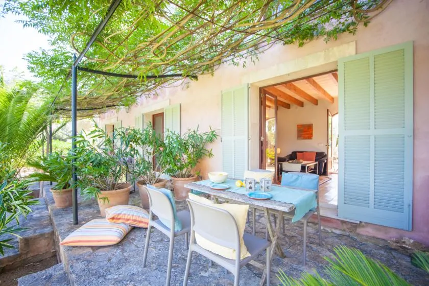 A shaded outdoor dining area with a table and chairs beside open doors.