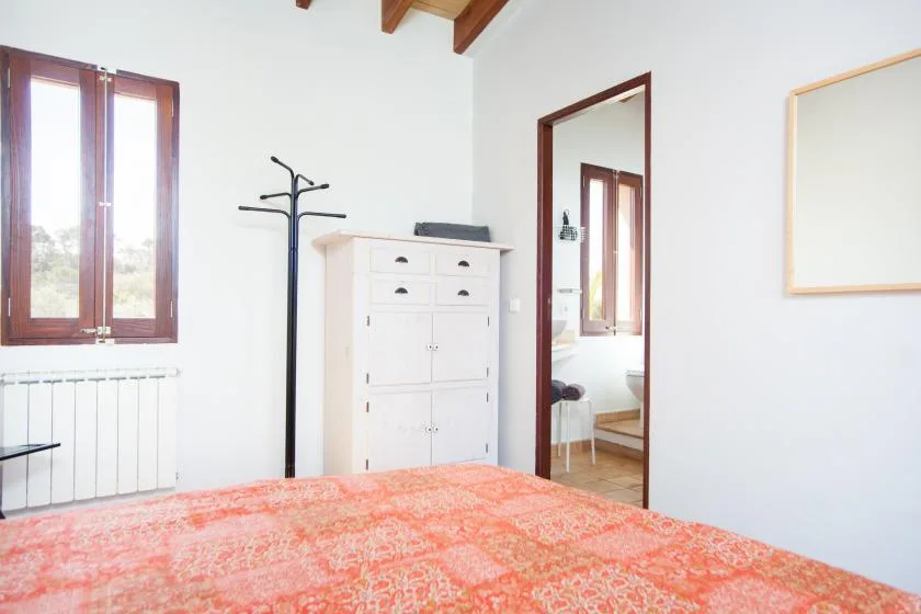 Un dormitorio con una colcha estampada, un armario blanco y una ventana con marco de madera.