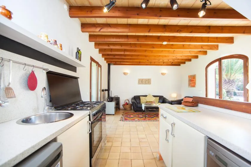 Una cocina luminosa se abre a una pequeña sala de estar, con vigas de madera en el techo.