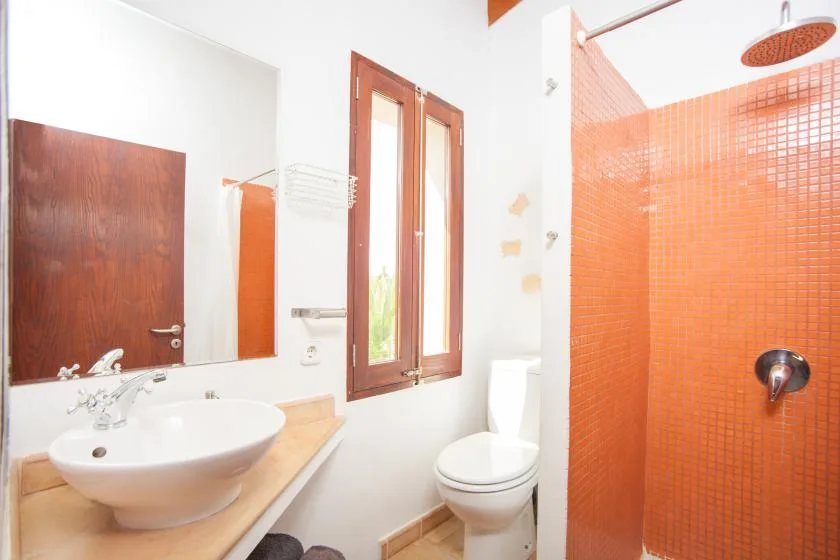 Un baño luminoso con lavabo, inodoro y ducha con azulejos naranjas.