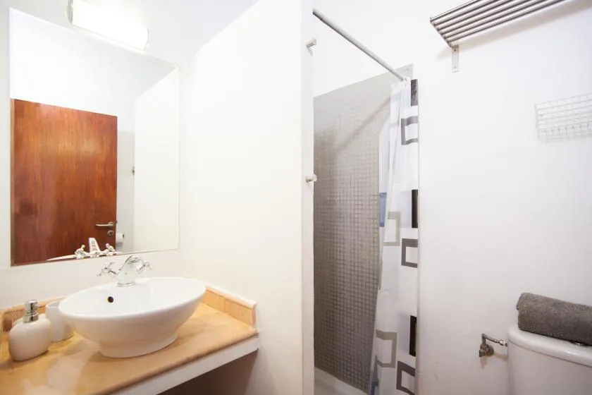 Un baño luminoso con lavabo, espejo y cortina de ducha estampada.