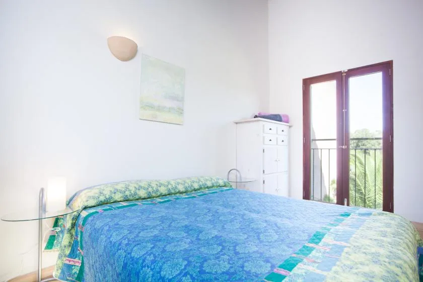 Un dormitorio con una cama cubierta con ropa de cama azul estampada junto a una puerta abierta al balcón.