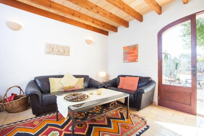 Sala de estar con asientos oscuros, una alfombra estampada y una puerta de vidrio que da a un patio.