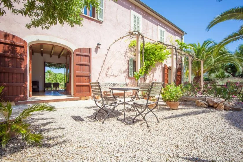 Un patio de grava con asientos al aire libre junto a un edificio rosado con puertas de madera abiertas.
