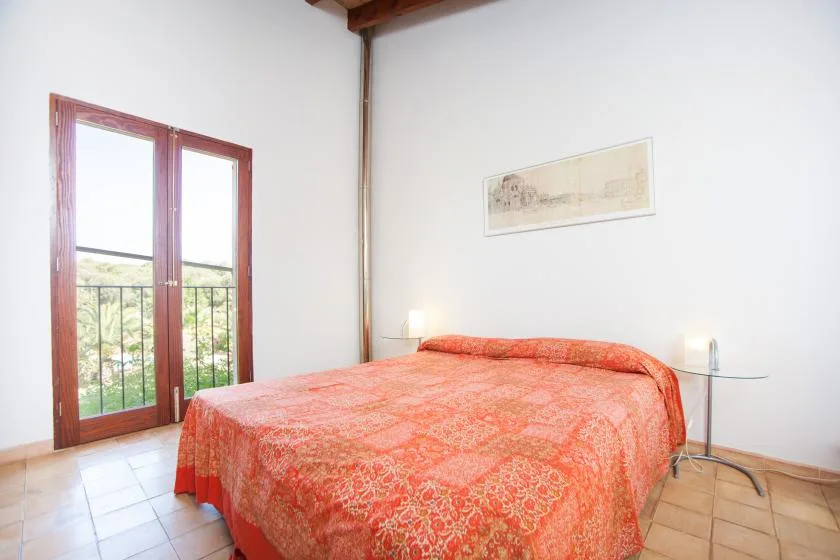 Un dormitorio con una cama cubierta con una colcha roja estampada junto a puertas acristaladas.