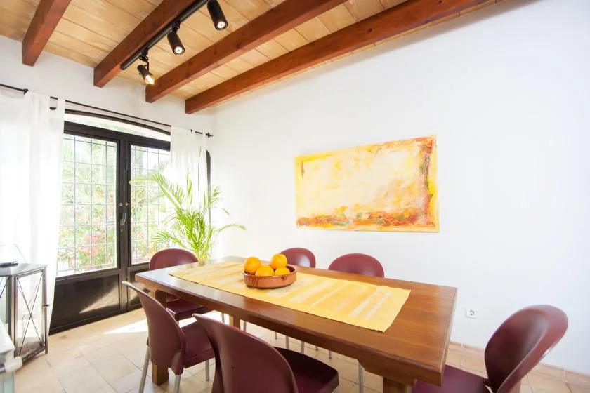Un comedor luminoso con una mesa de madera, sillas y grandes ventanas.