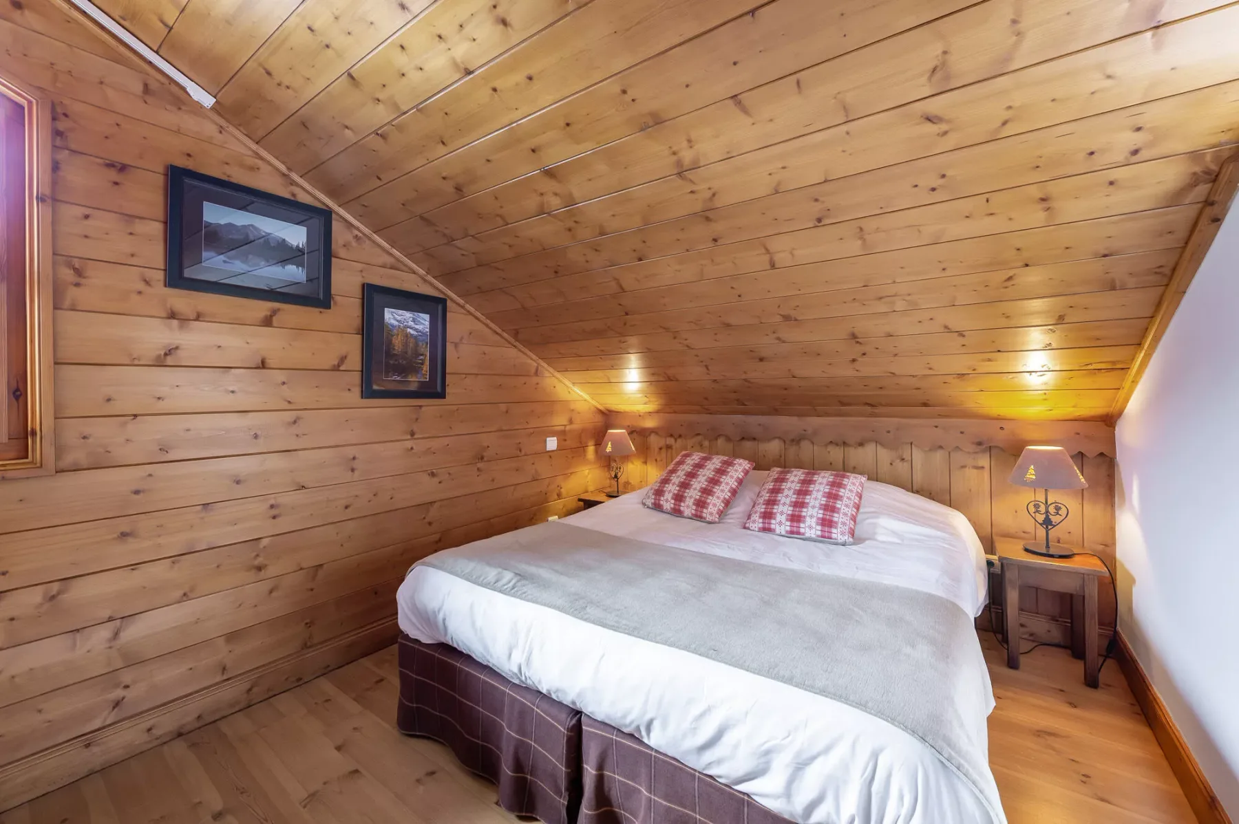 A bedroom with a large bed beneath a sloped wooden ceiling.
