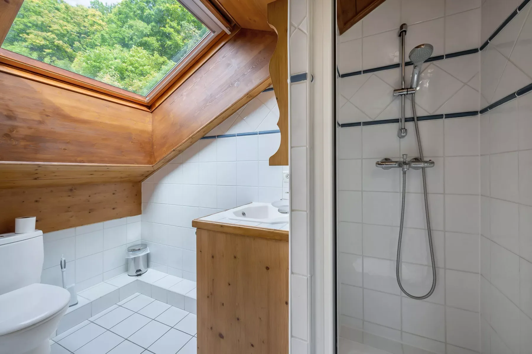 Un baño alicatado con ducha, lavabo y techo de madera inclinado.