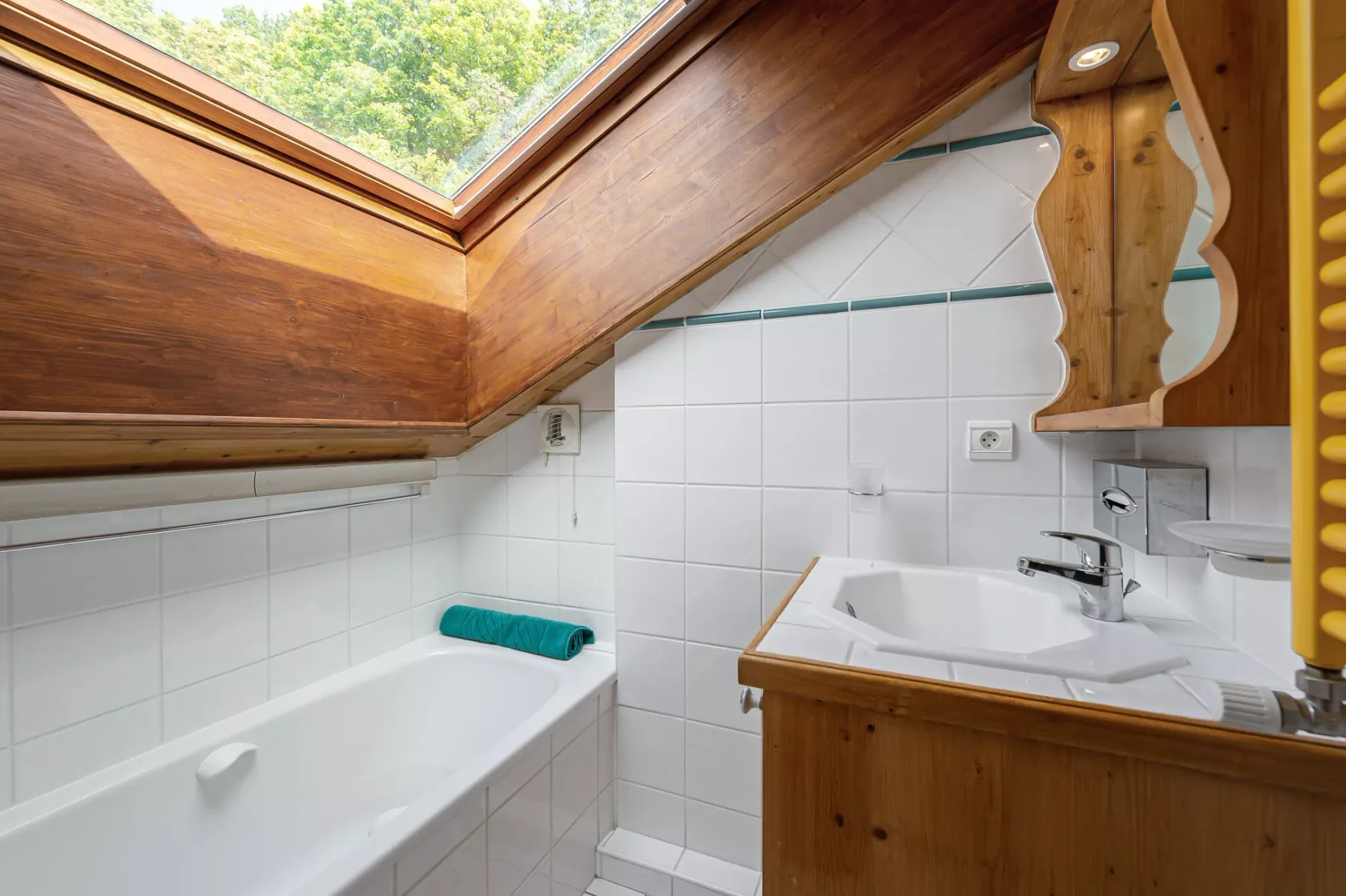 A tiled bathroom has a bathtub and a sink beneath a sloped wooden ceiling.