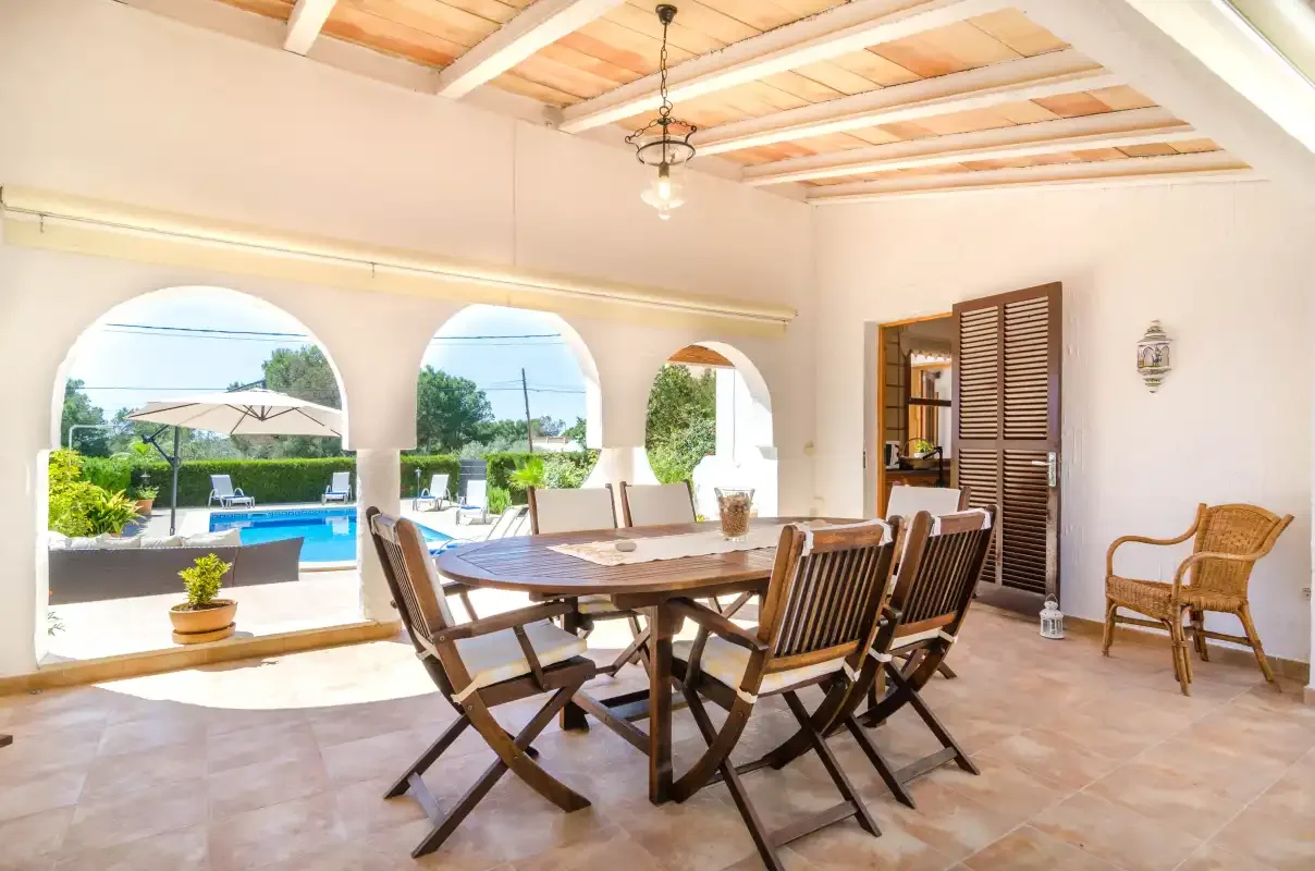 A dining area with a wooden table and chairs opens onto a poolside view.