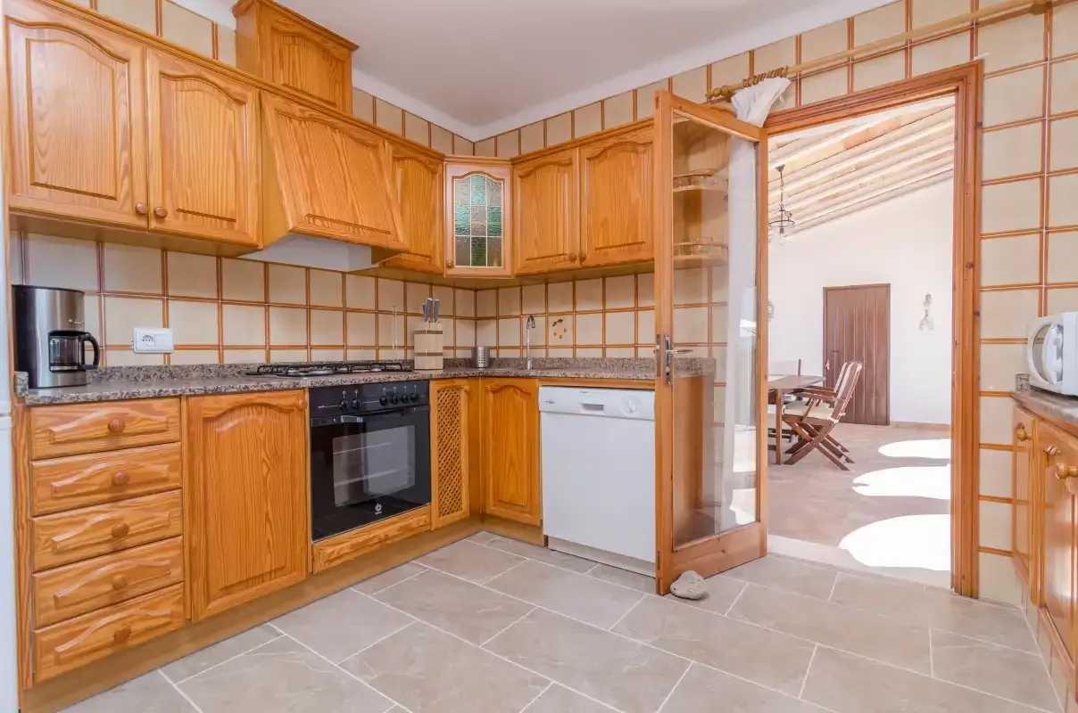 A kitchen with wooden cabinets, tiled counters, and an open doorway.