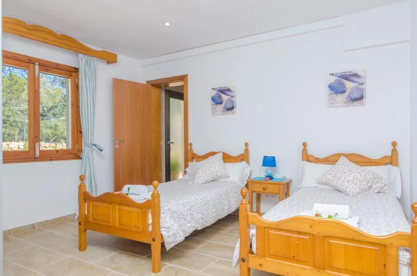 A bright bedroom with two wooden beds and a window overlooking greenery.