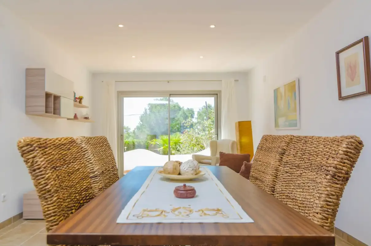 Dining area with a wooden table and woven seating beside a large glass door.