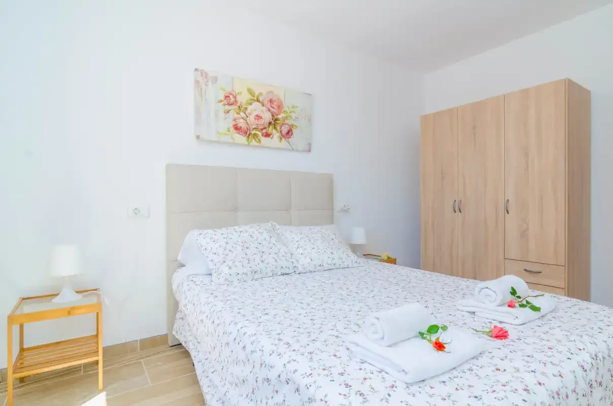A bedroom with a bed, floral bedding, and a wooden wardrobe.