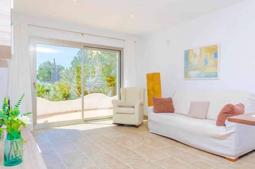 A bright living room has a white sofa beside a large glass sliding door.