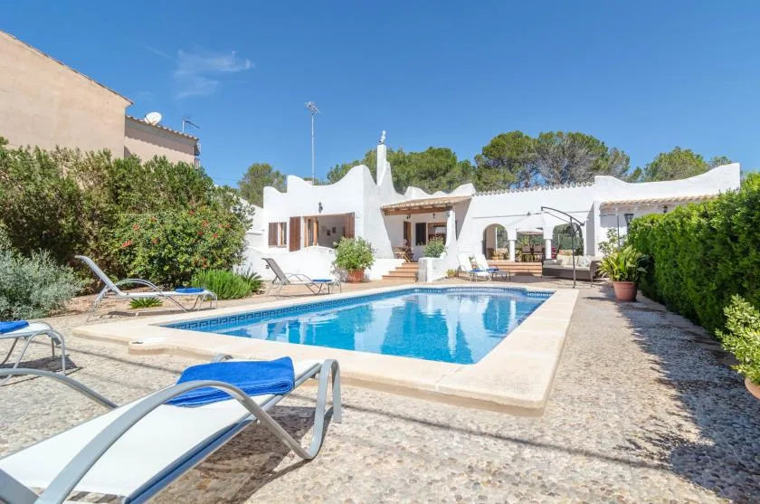 A swimming pool sits in a sunny courtyard beside a white building.