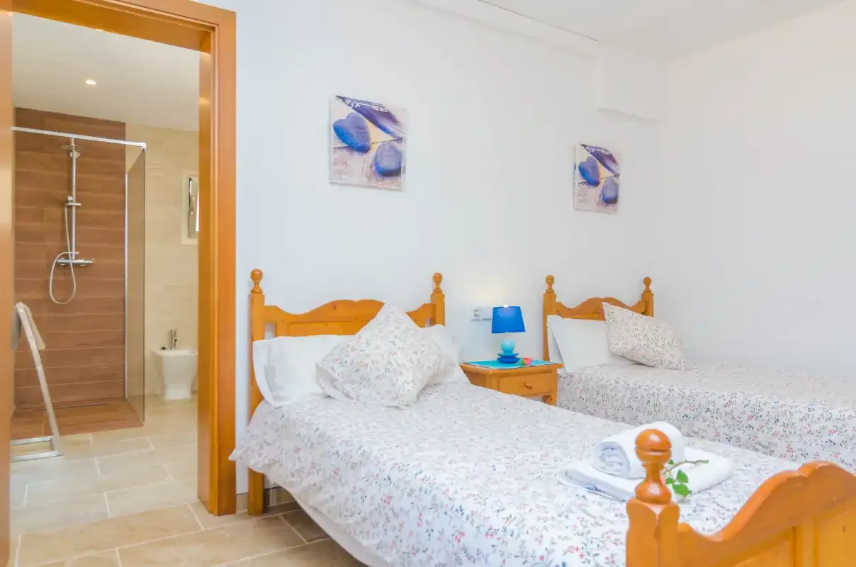 A bedroom with two beds and a bathroom visible through the open doorway.