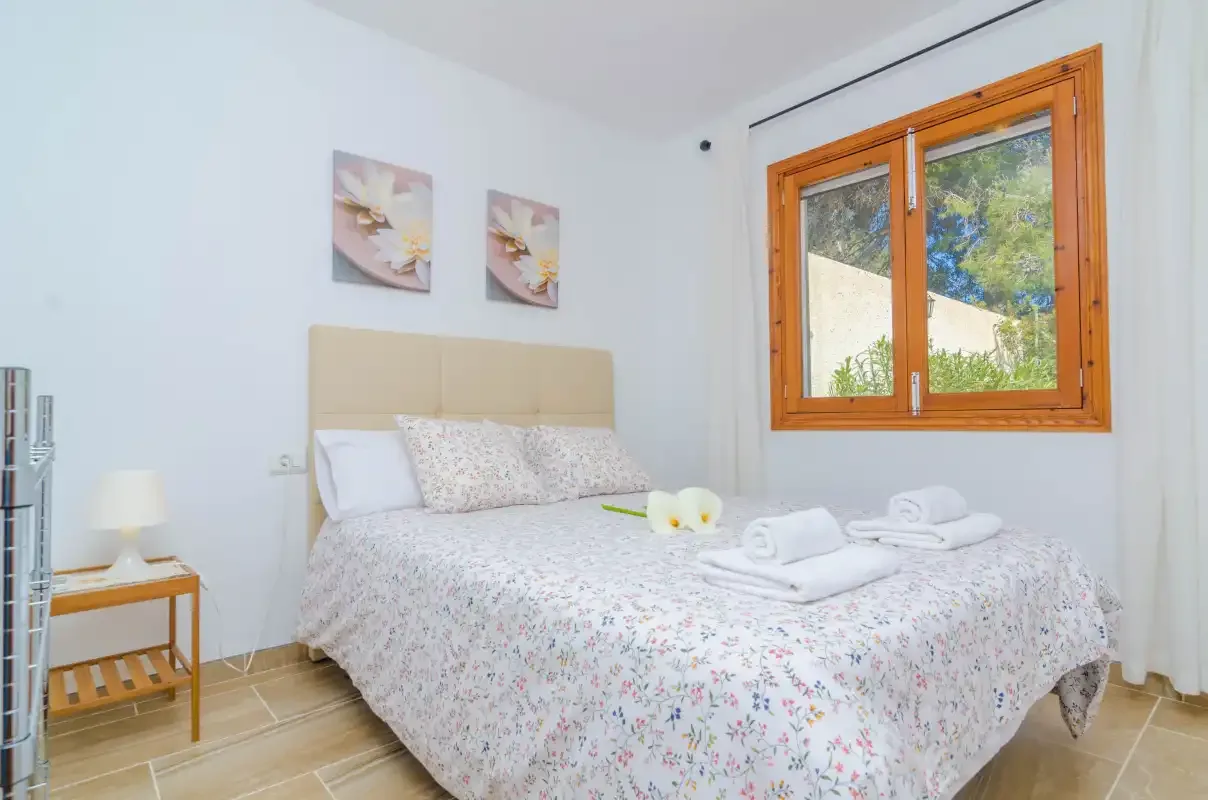A bright bedroom with a double bed and a wooden-framed window.