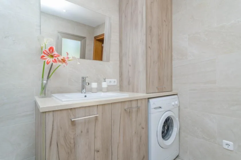 A bathroom vanity with a sink, mirror, and washing machine.
