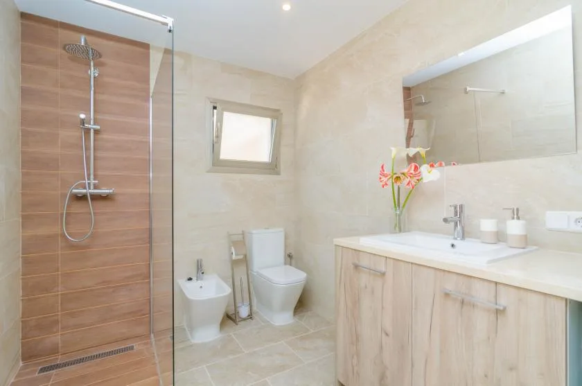 A bright bathroom with a glass shower, toilet, and vanity.