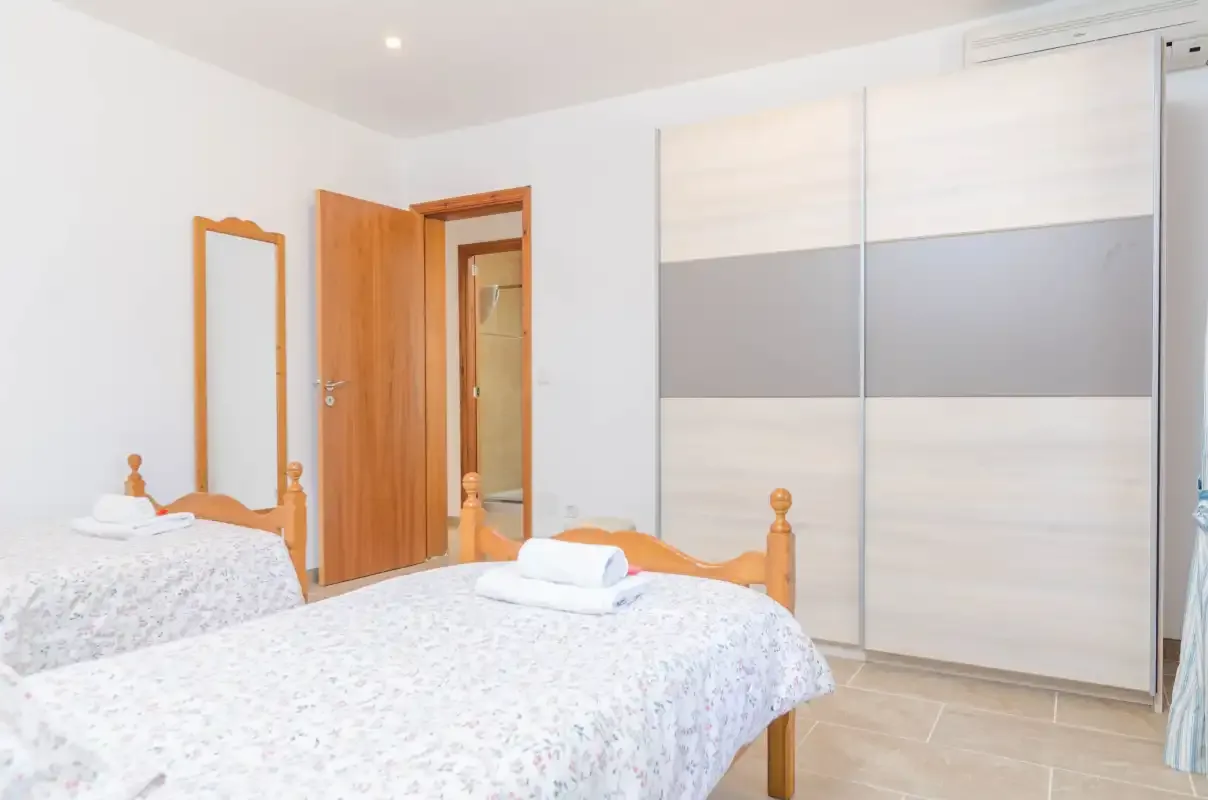 A bright bedroom with two beds and a large sliding-door wardrobe.