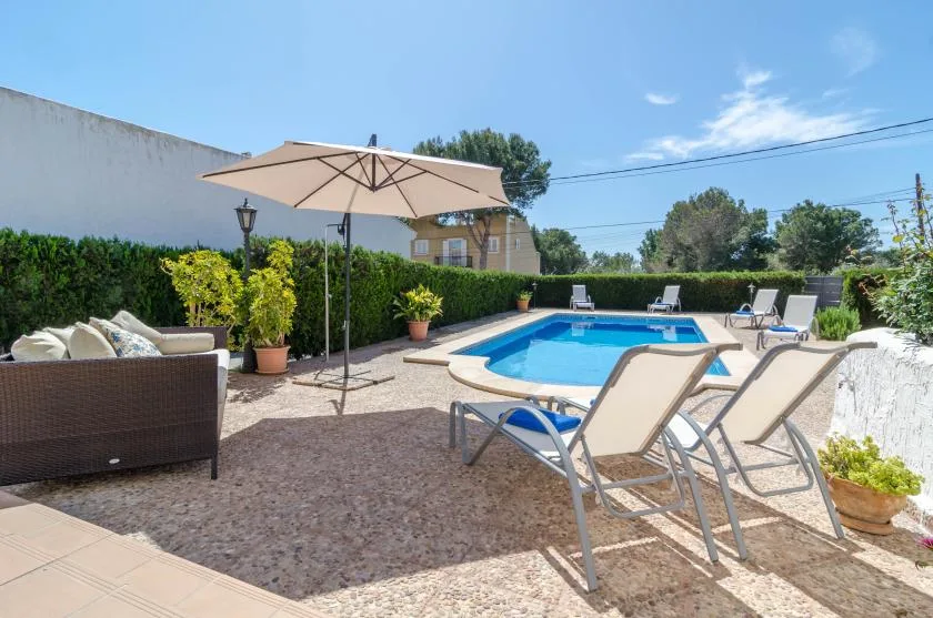 An outdoor swimming pool sits beside a paved patio with loungers and an umbrella.