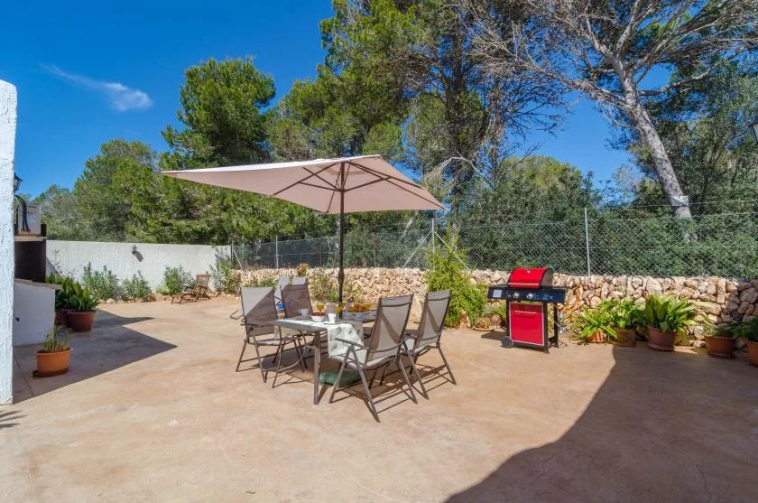 An outdoor patio with a dining table, umbrella, and grill.