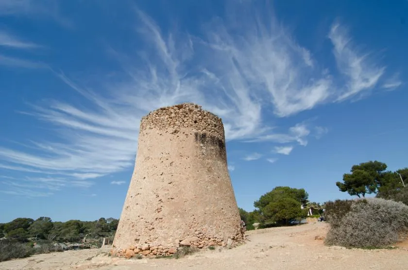 A stone tower stands in an open landscape beneath a blue sky.
