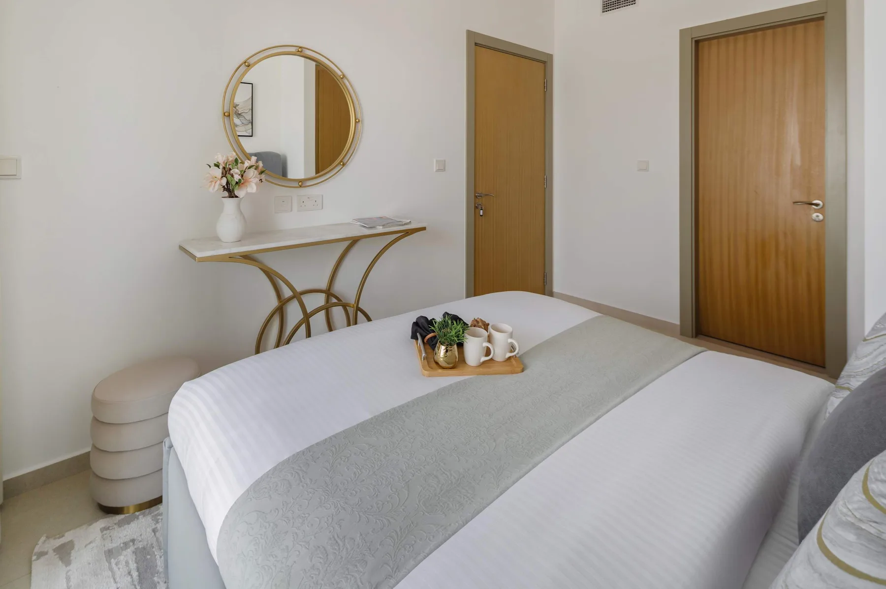 A bedroom with a neatly made bed and a console table beneath a round mirror.