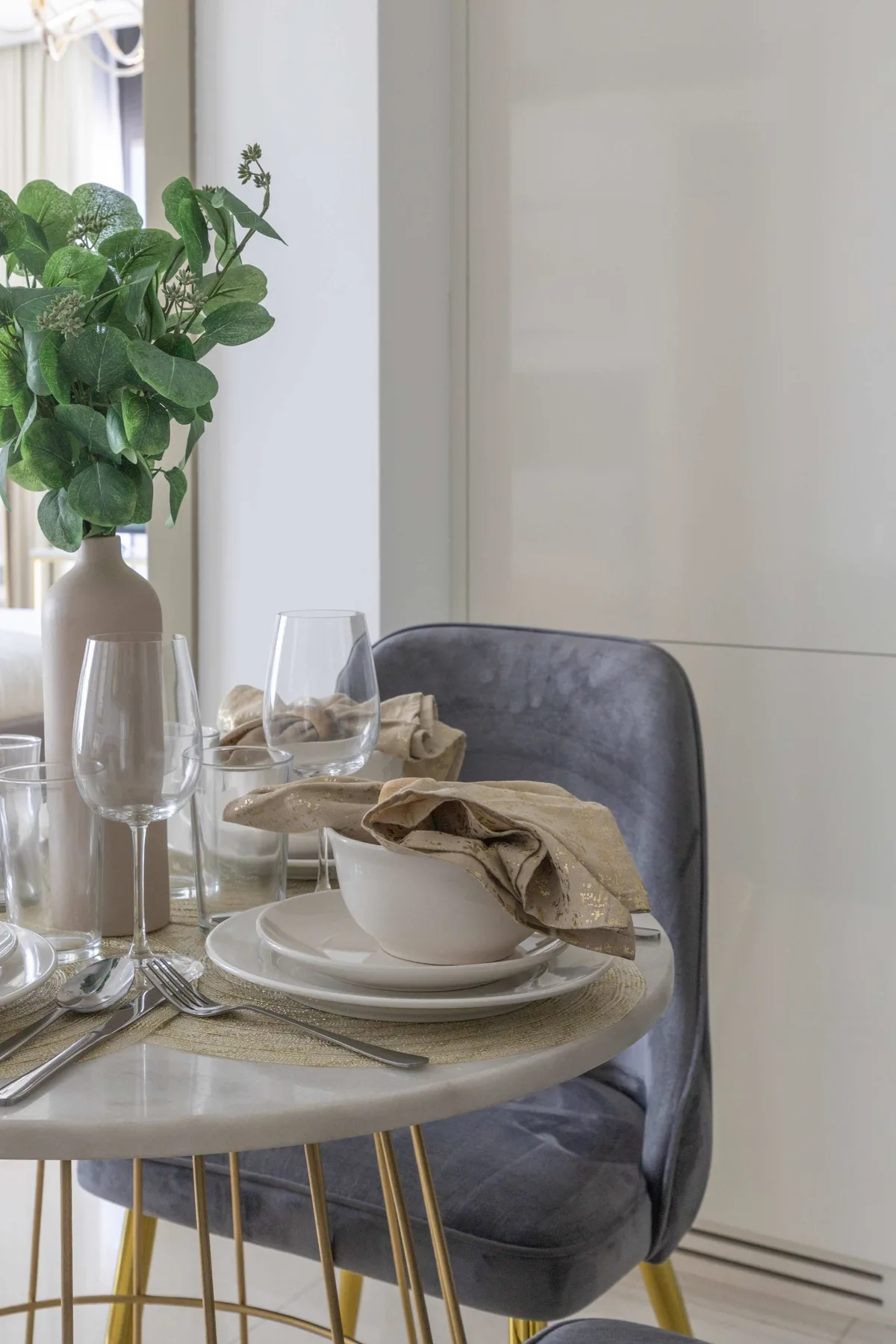 A dining table is set with dishes and glasses beside a leafy plant.