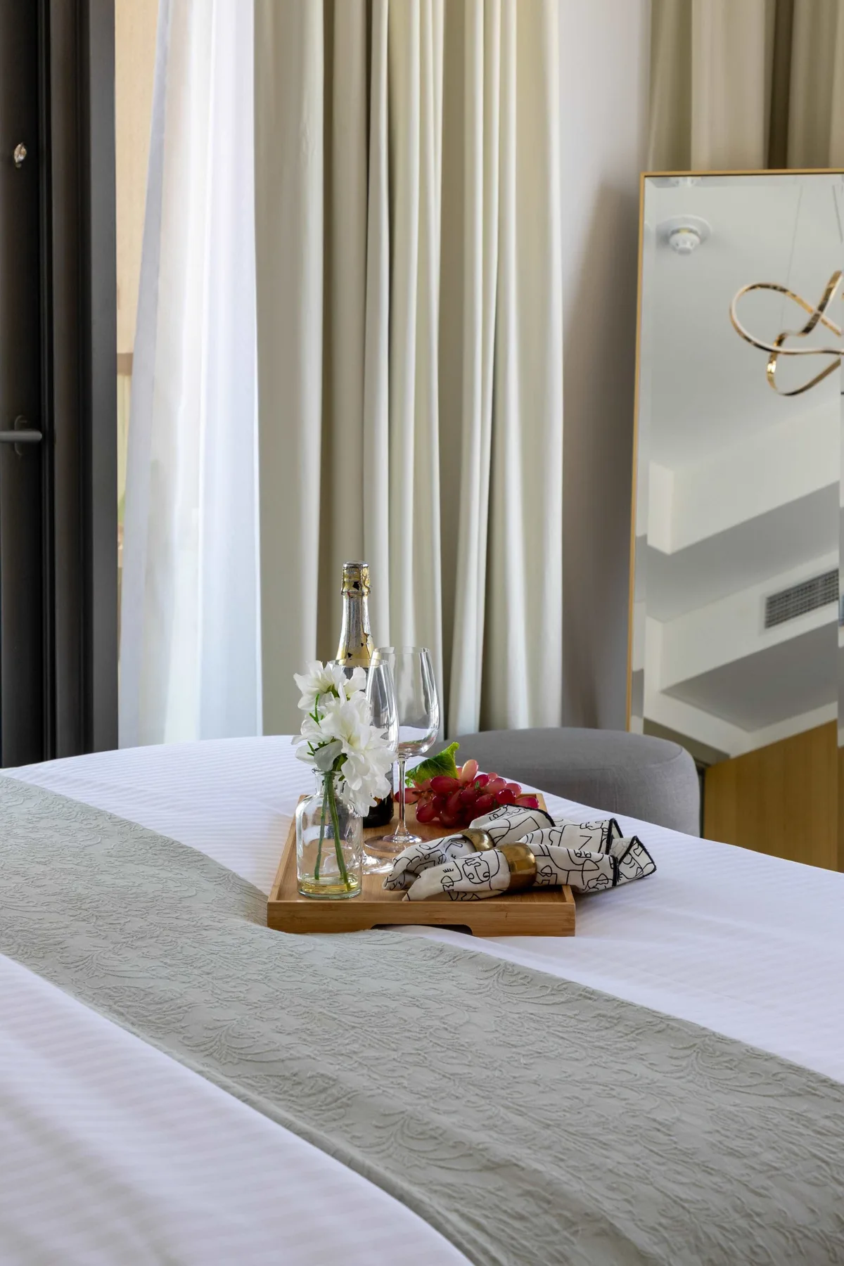 A neatly made bedroom bed with a tray of flowers and drinks.