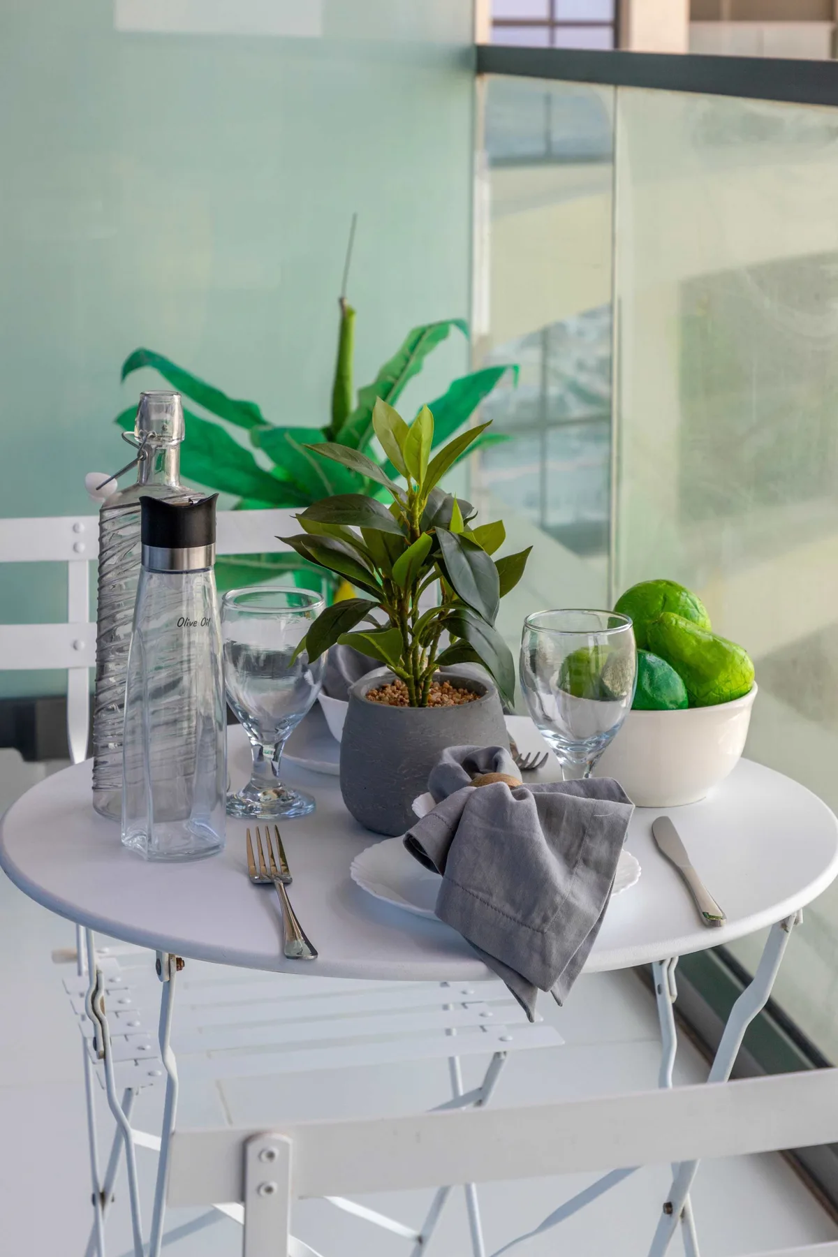A small dining table is set with glasses, cutlery, and potted plants.