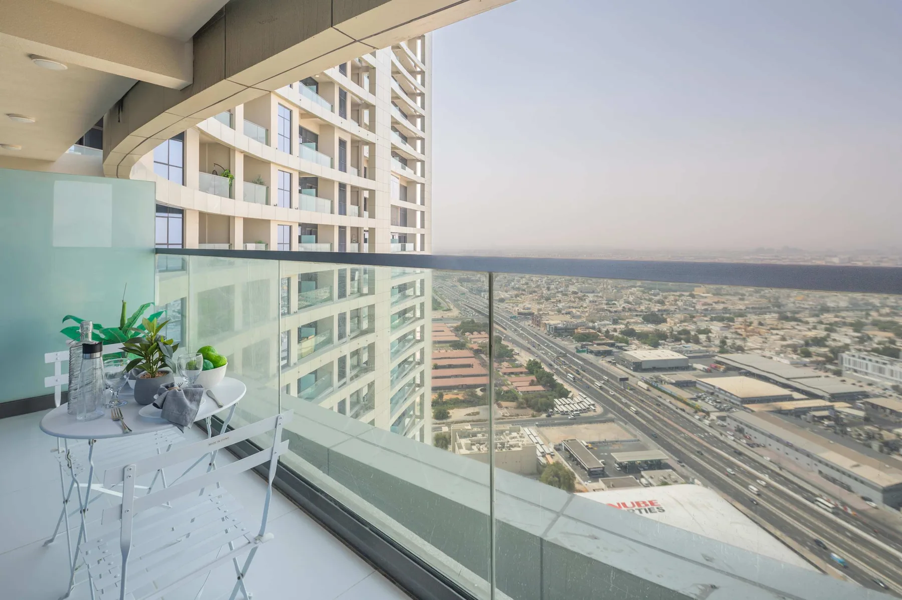 A balcony with glass railing and seating overlooks a cityscape.