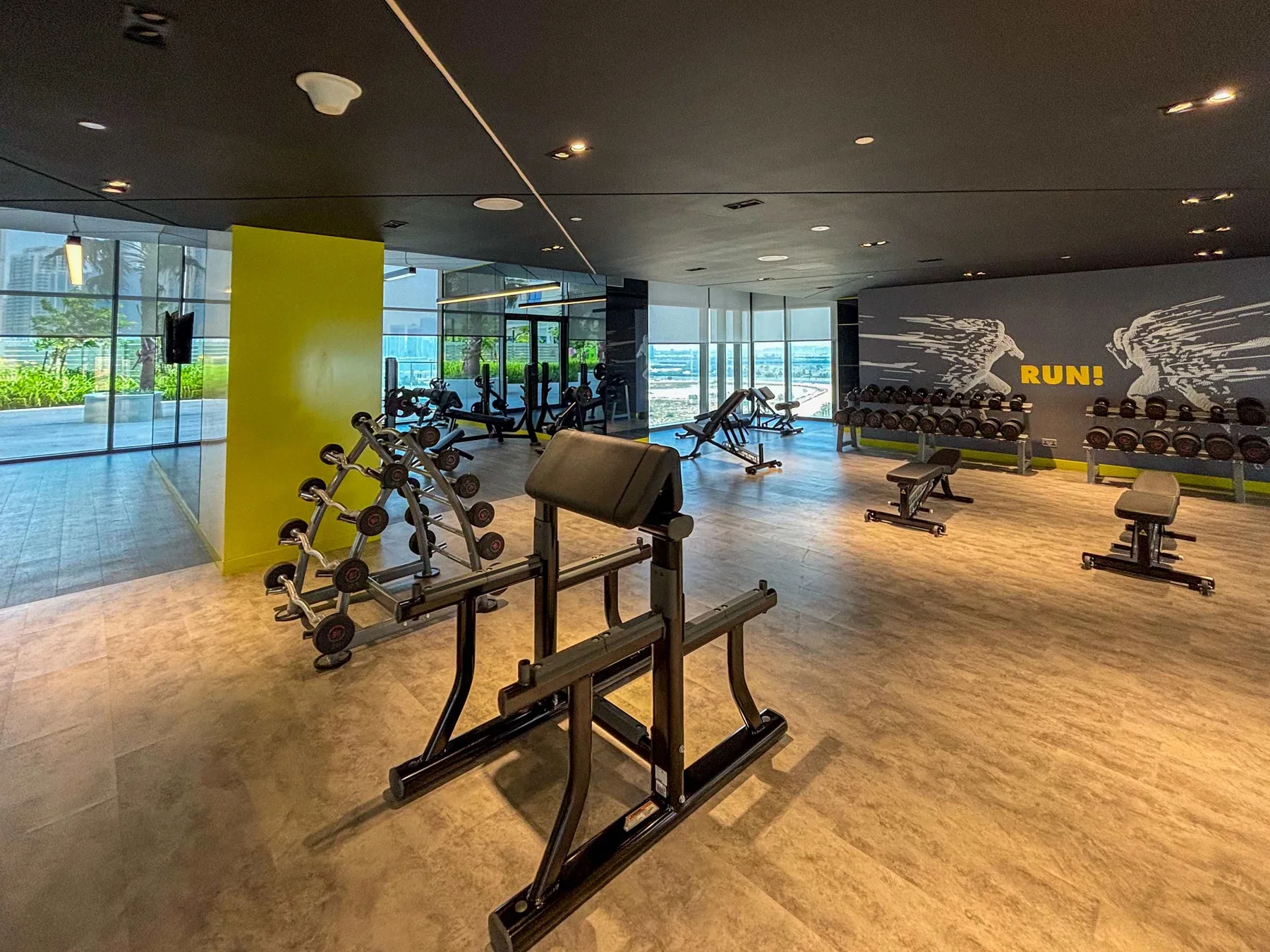 A gym with exercise machines, free weights, and floor-to-ceiling windows.