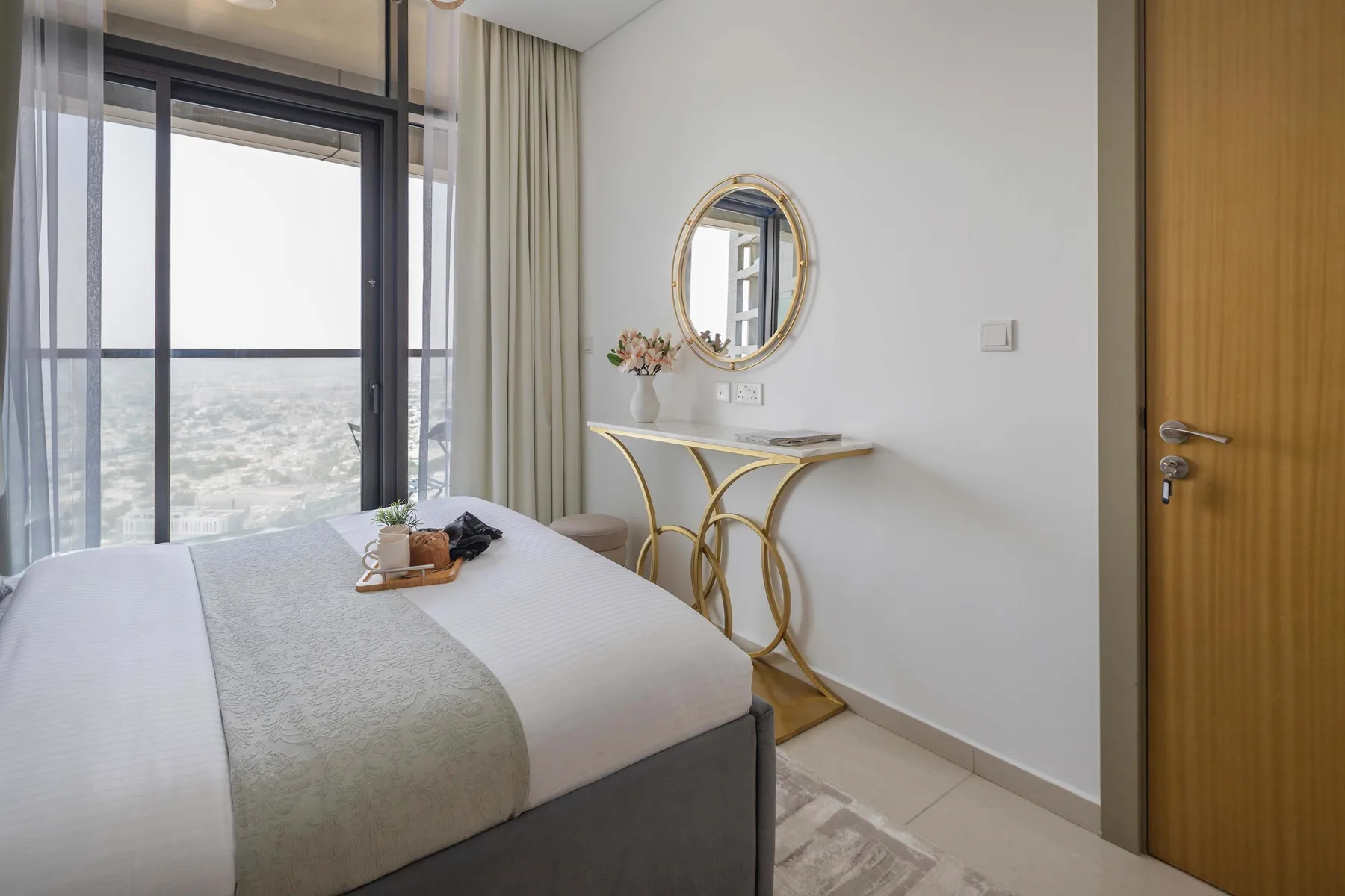 A bedroom with a bed beside a large window and a small vanity table.