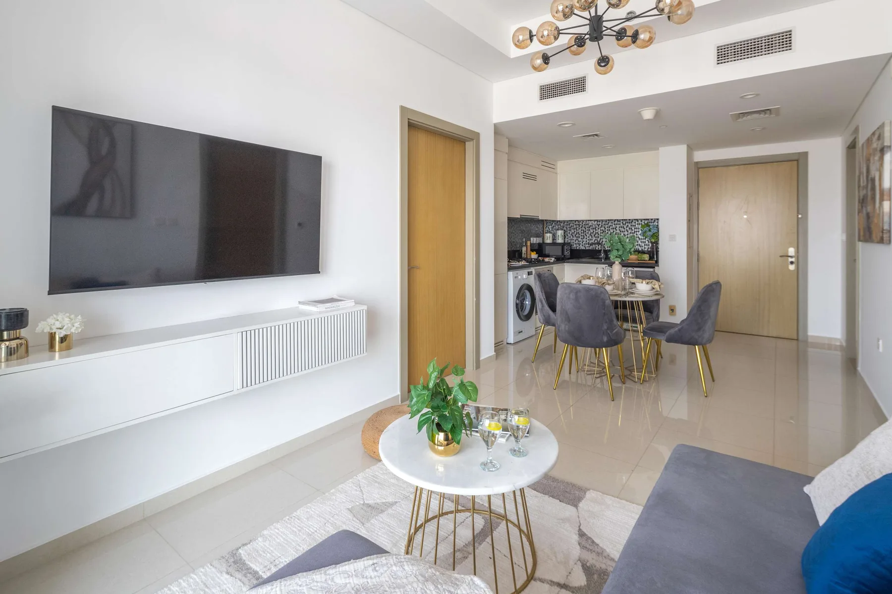 A bright living and dining area opens onto a compact kitchen, with a wall-mounted television.