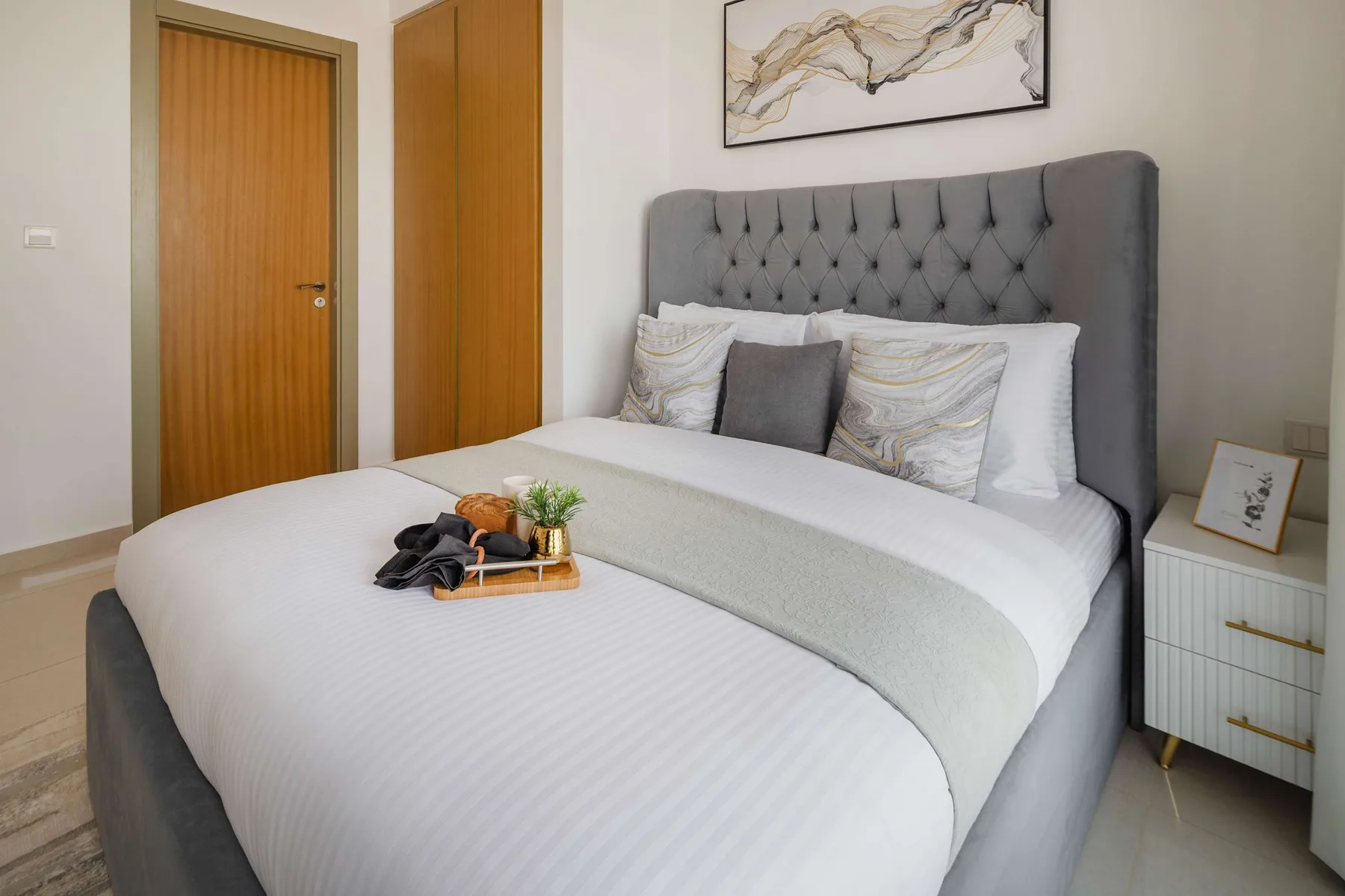 A bedroom with a neatly made bed and a framed abstract artwork above the headboard.