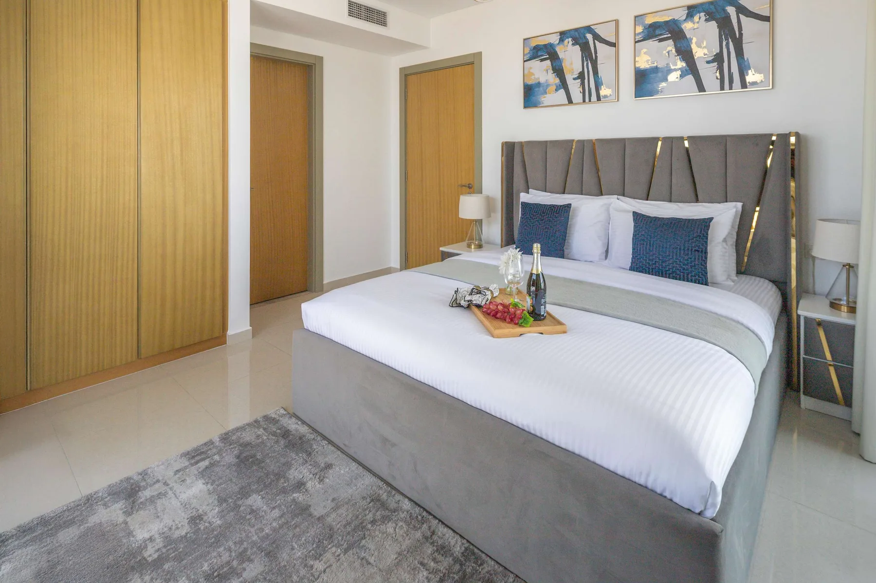 A bedroom with a neatly made bed, bedside tables, and abstract wall art.