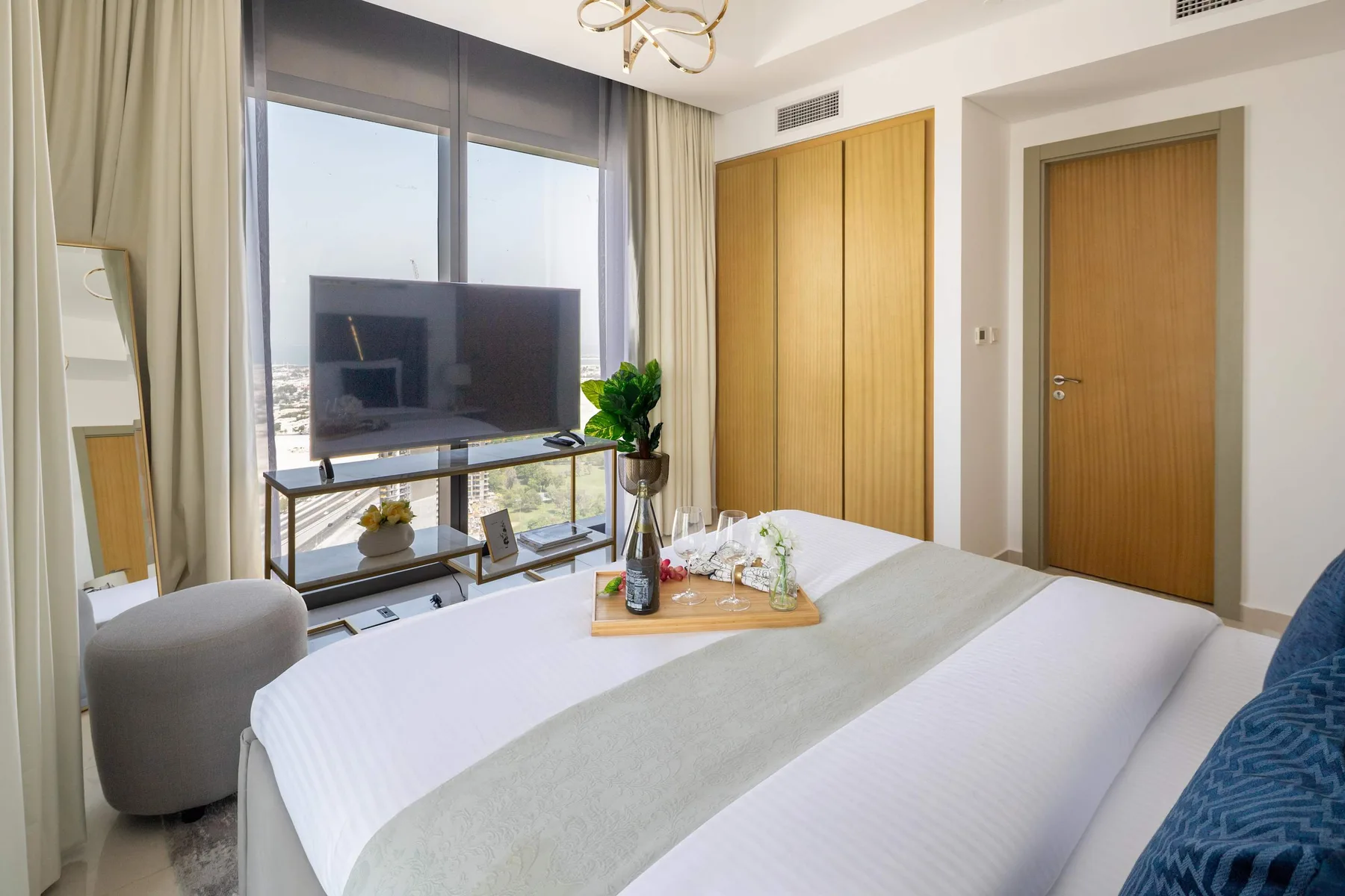 A bedroom with a neatly made bed, television, and large windows.