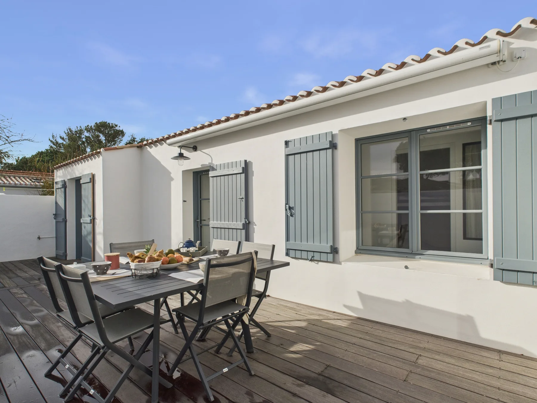 A sunny outdoor dining area beside a white house with pale blue shutters.