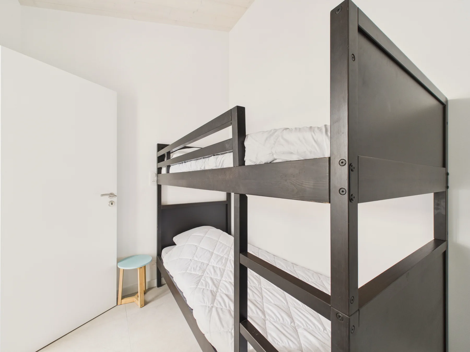 A bunk bed with white bedding stands in a bright bedroom.
