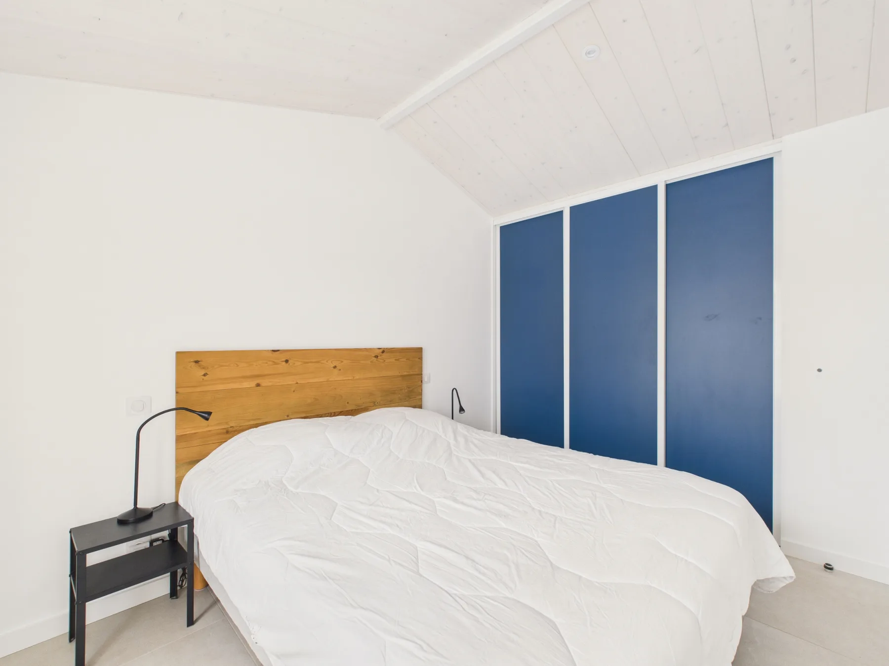 A bright bedroom with a bed beneath a sloped white ceiling.