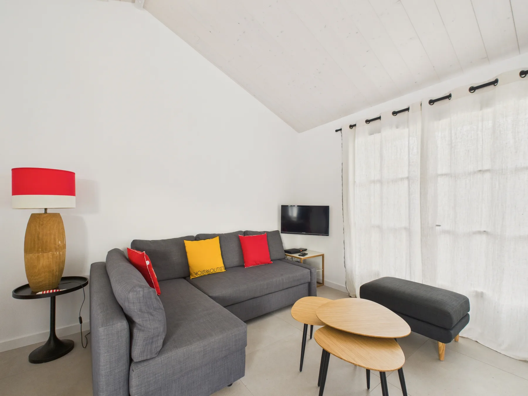 A bright living room with gray seating, colorful cushions, and a television.