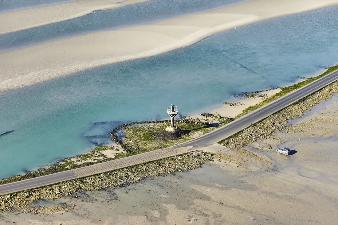 Aerial view of a coastal road beside shallow water and sandbanks.