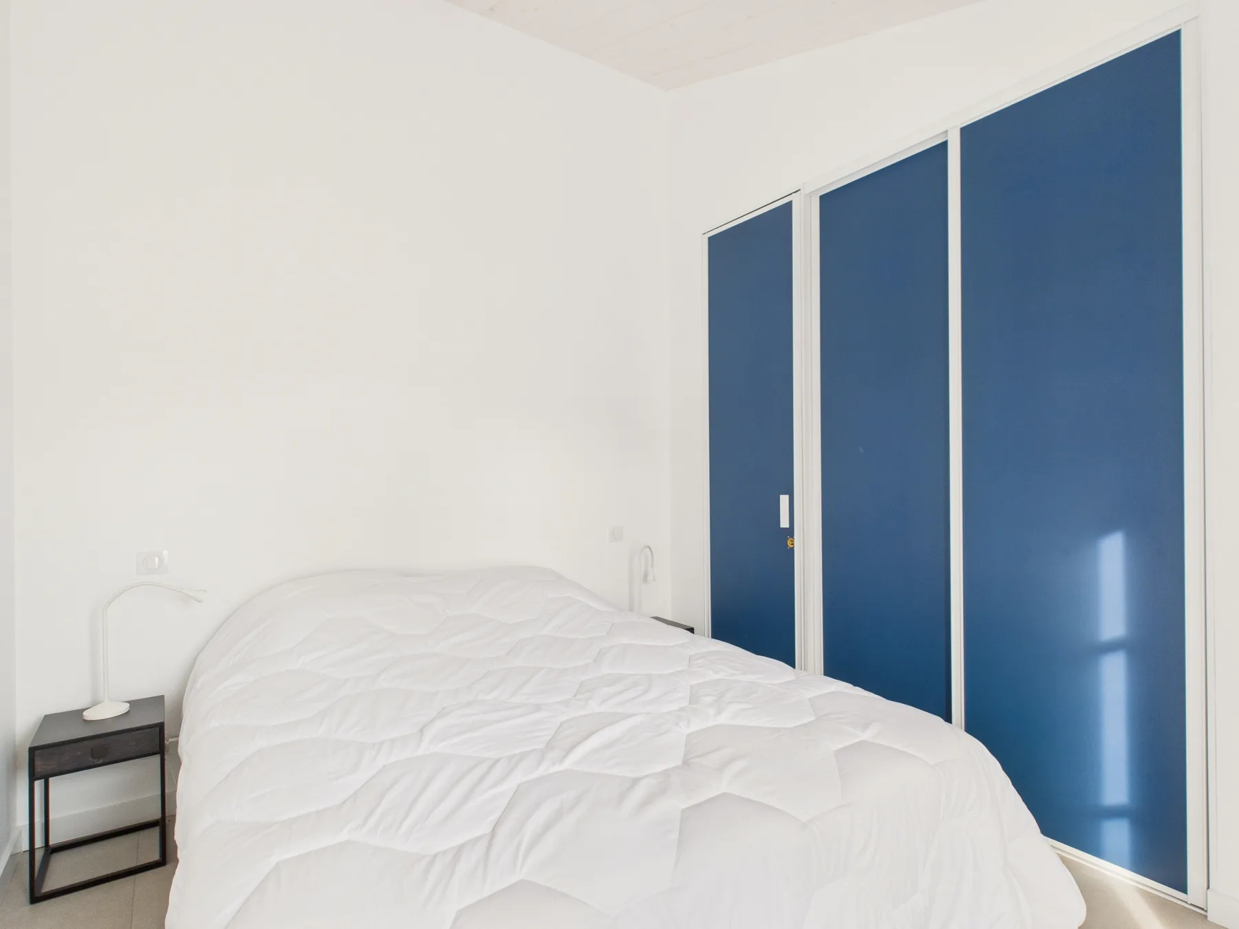 A bright bedroom with white bedding and blue wardrobe doors.