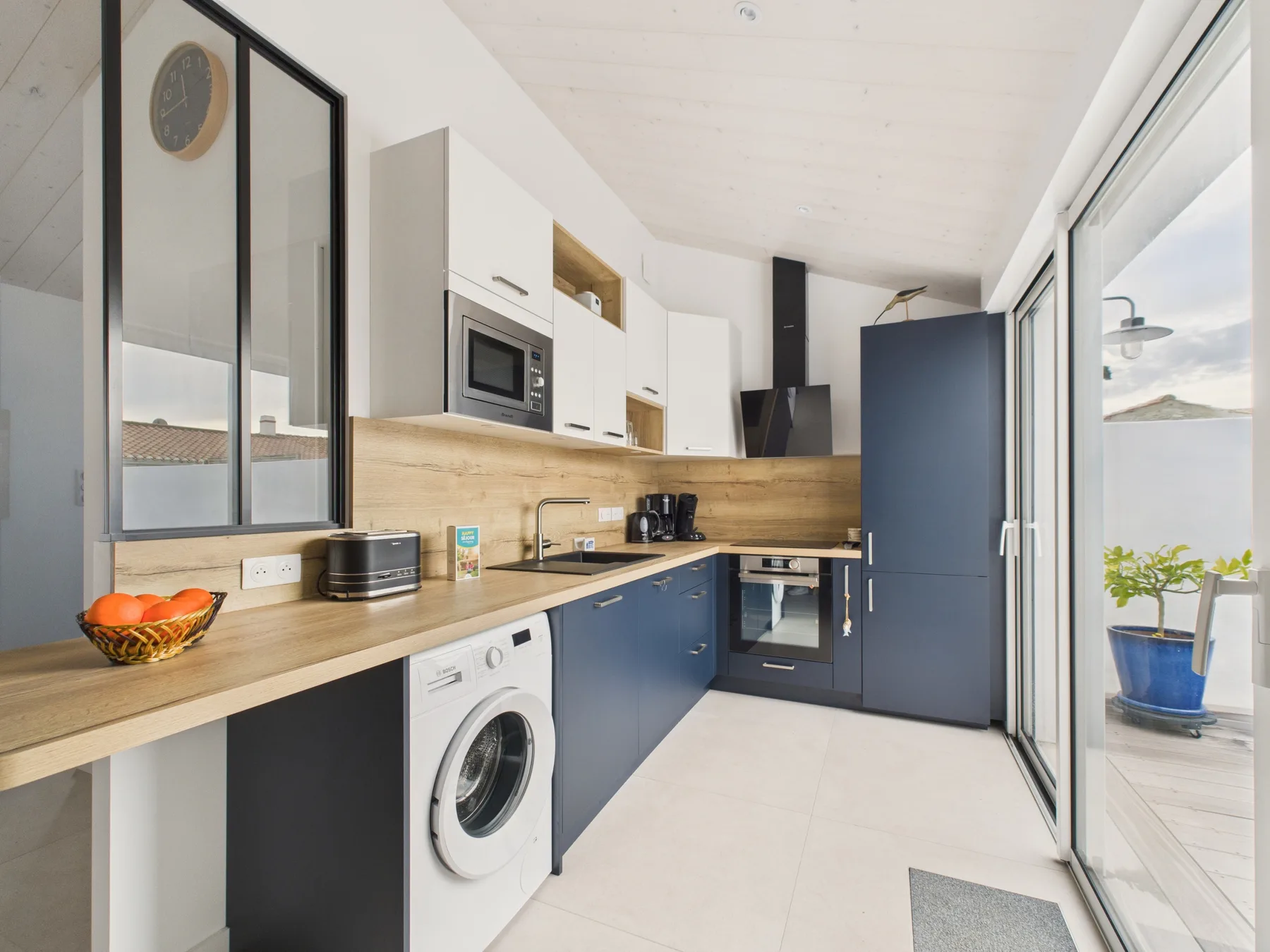 A modern kitchen with blue cabinets, a washing machine, and sliding glass doors.