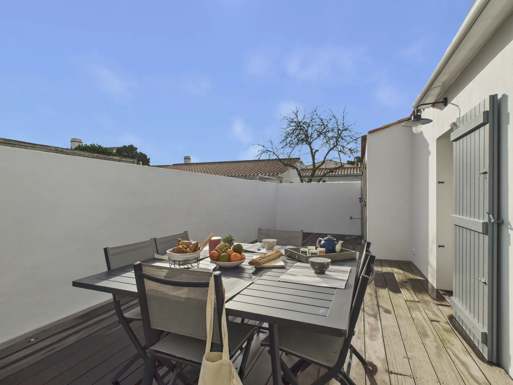 An outdoor dining area with a table and seating beside a white wall.